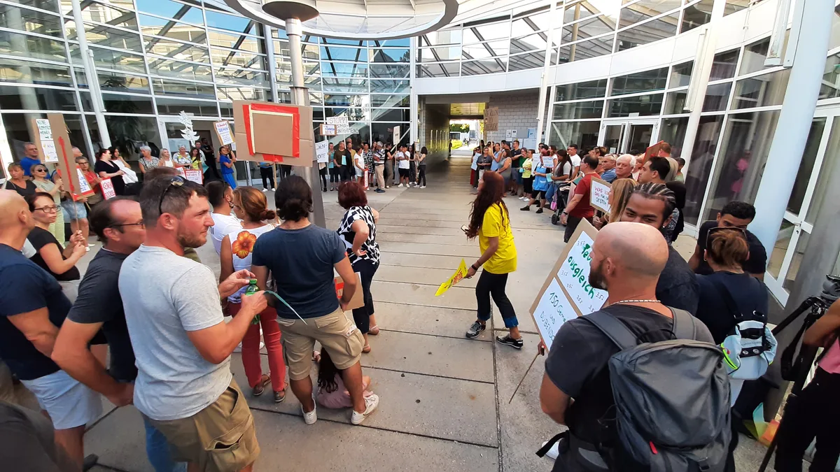 Mehrere Personen mit Plakaten sind im Lichthof eines Gebäudes versammelt. 